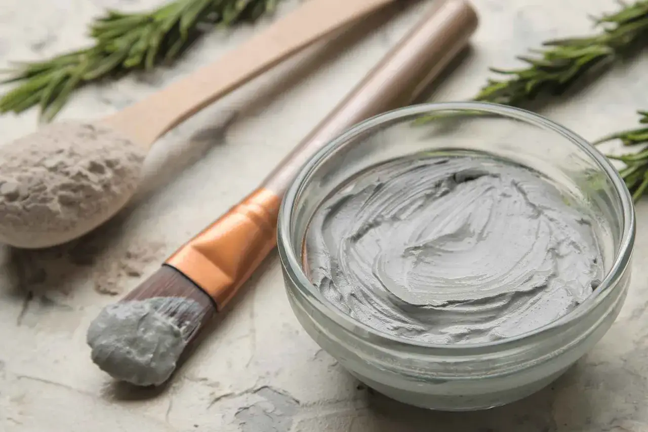 Maschera viso all'argilla: purifica e rigenera la pelle. Un cucchiaio di polvere, un pennello e una ciotola pronta per il trattamento.