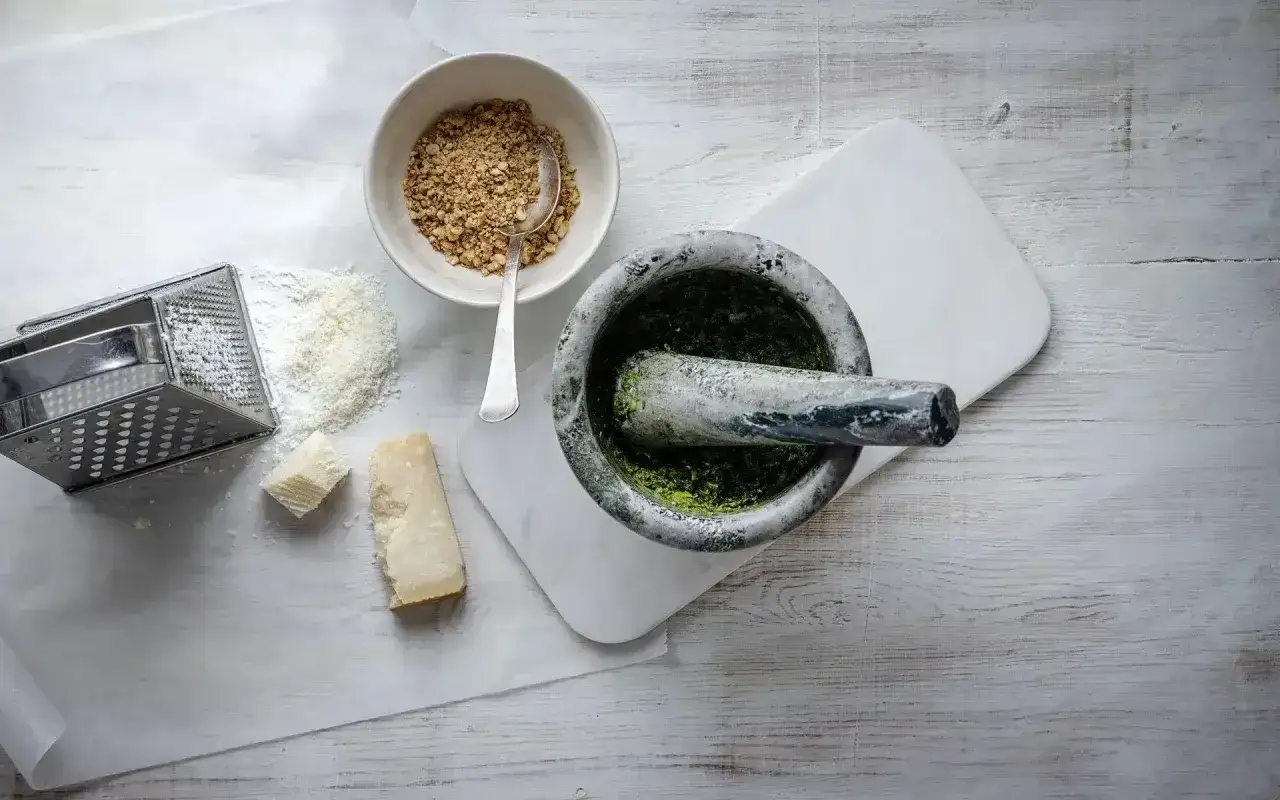 Mortel med grön pesto, riven parmesan, nötter och rivjärn. Ingredienser för ett klassiskt pesto recept.