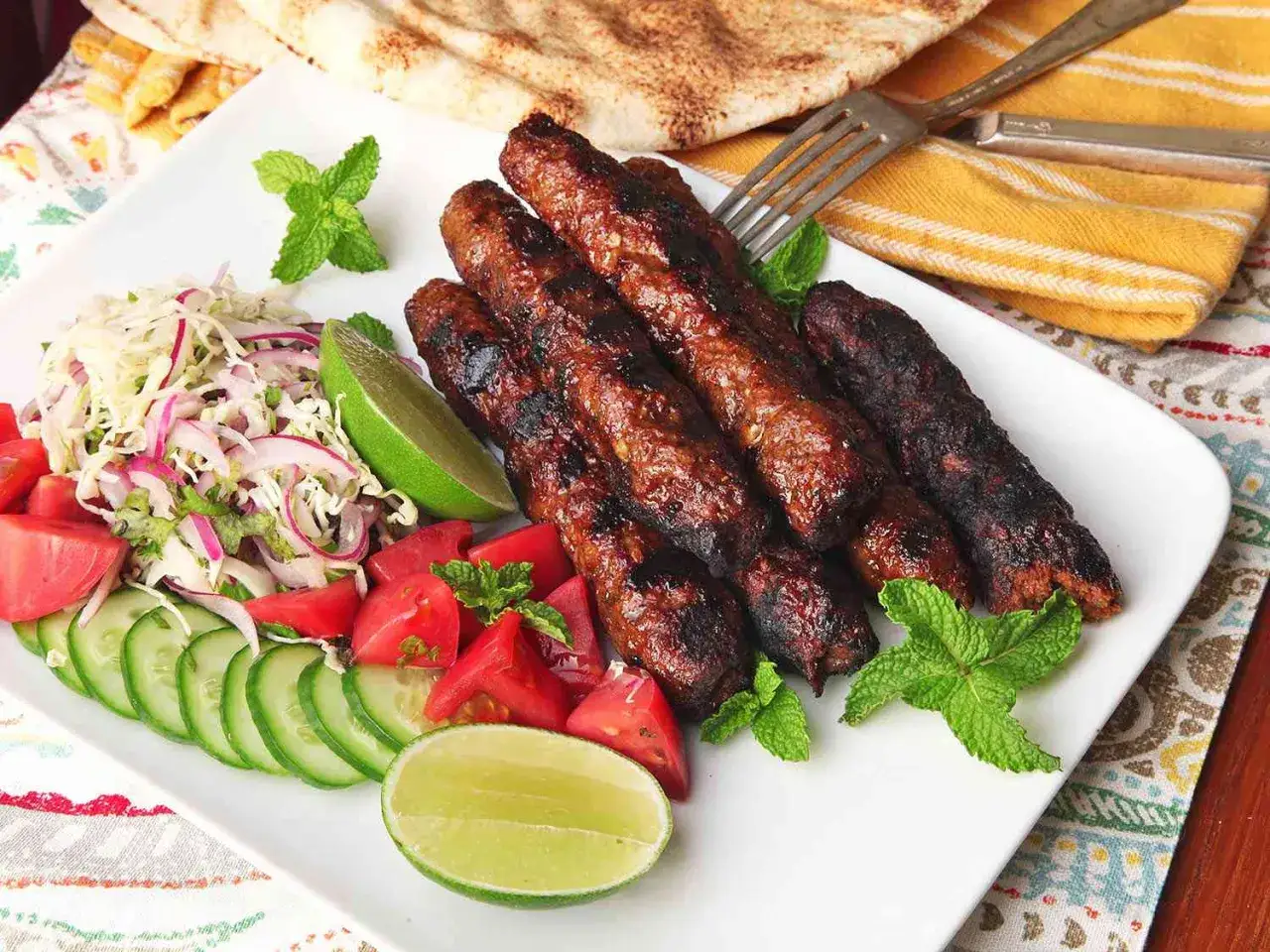 Grillowany kebab z mięsa mielonego, podany z sałatką z kapusty, pomidorów, ogórka, cebuli i limonki, ozdobiony miętą.