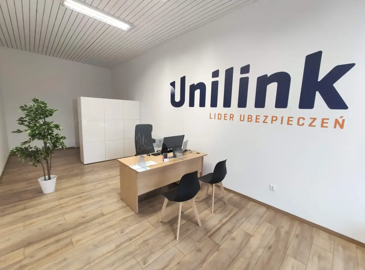 Wnętrze biura ubezpieczeniowego Unilink z biurkiem, krzesłami i rośliną.
