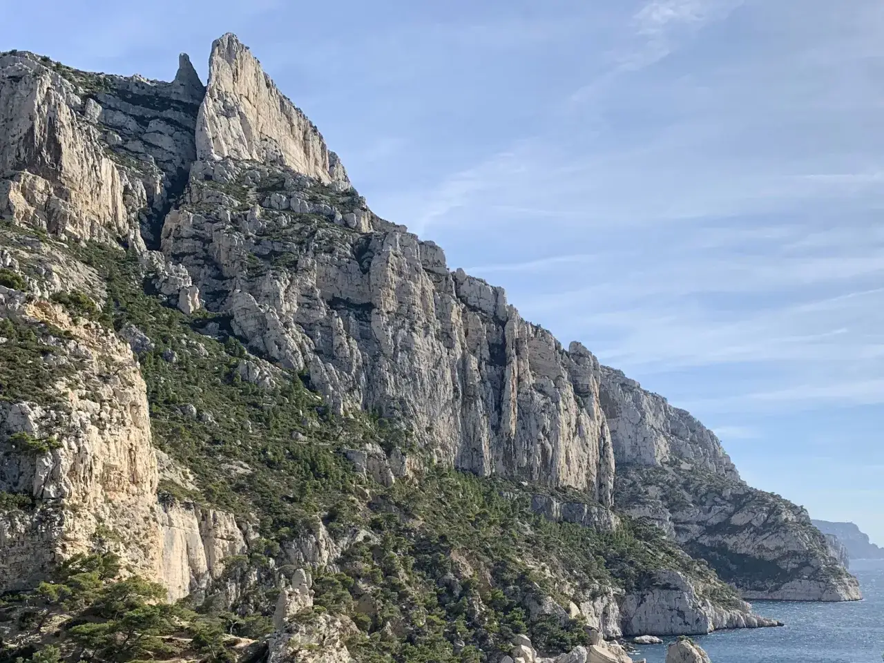 Le **Mont Puget** se dresse, imposant, ses falaises calcaires plongeant vers la mer bleue sous un ciel clair.