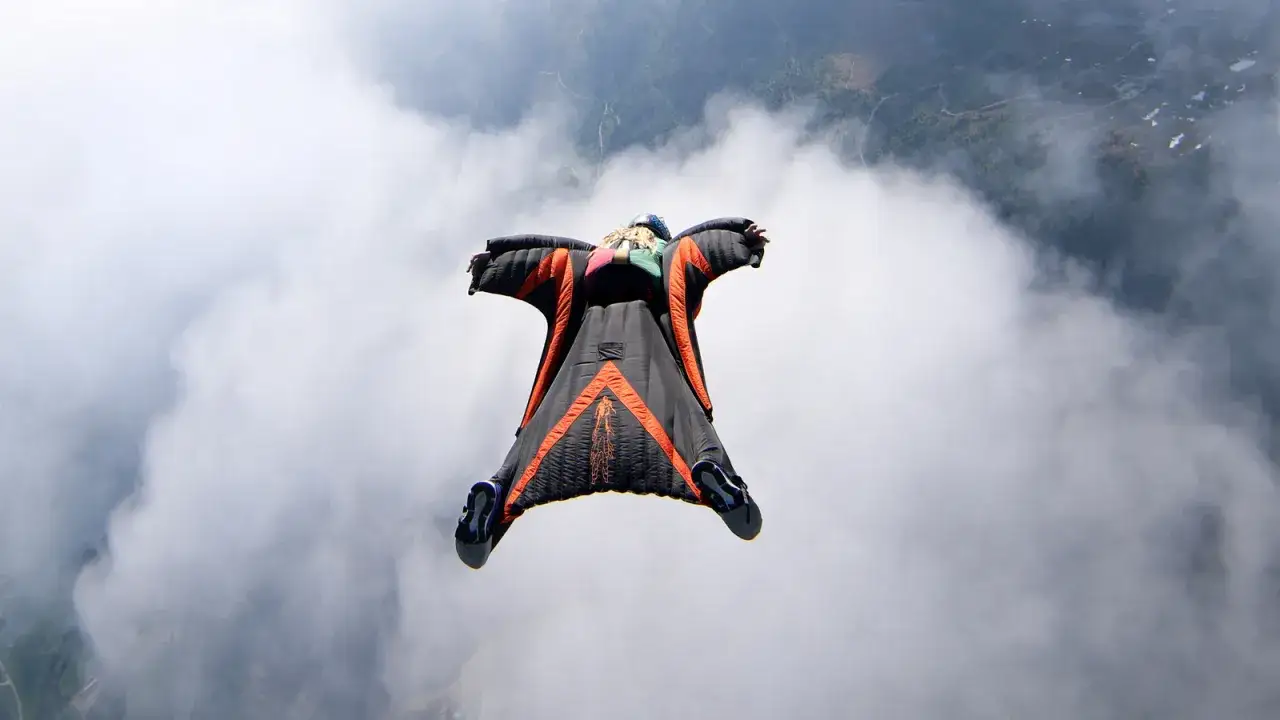 Człowiek w kombinezonie wingsuit szybuje przez chmury, szukając kolejnej dawki adrenaliny.