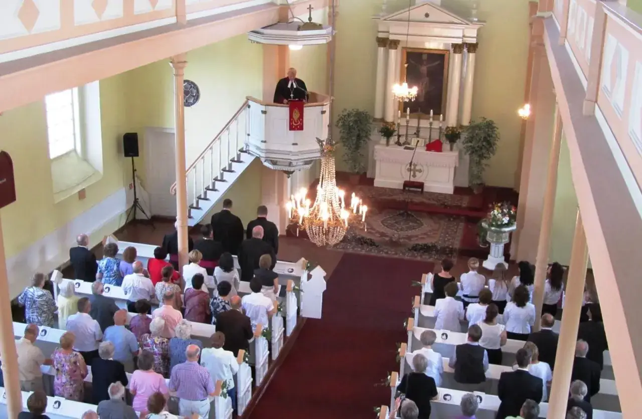 Nabożeństwo w kościele ewangelicko-augsburskim. Kazanie wygłasza pastor. Wierni słuchają w ławkach. To jest luteranizm.