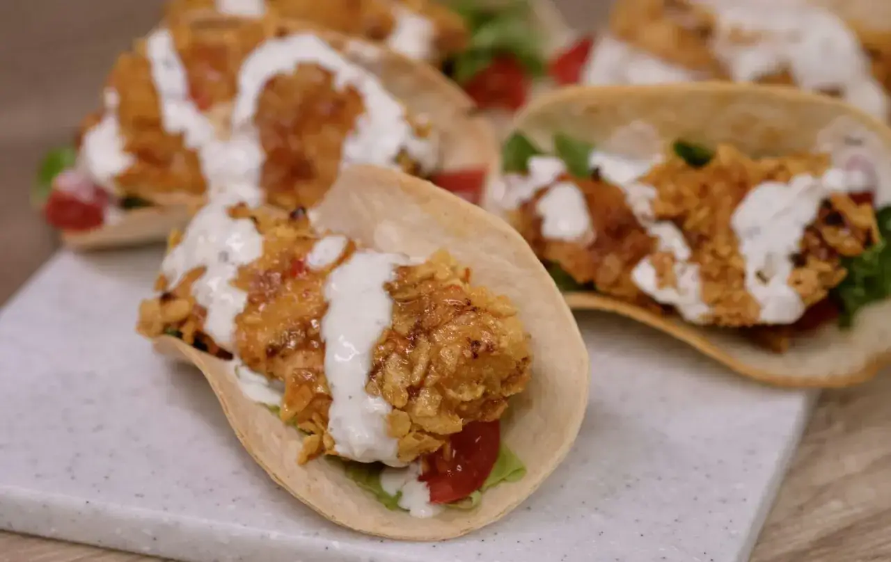 Pyszne tacos z kurczakiem w panierce, polane kremowym sosem, z dodatkiem świeżych warzyw.