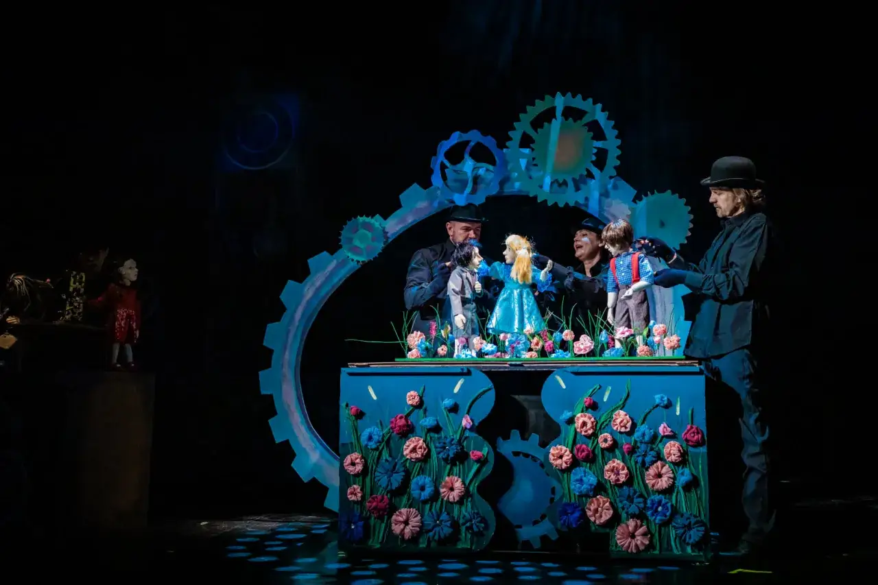 Teatr animacji repertuar: kukiełki ożywione przez aktorów na tle scenografii z kołami zębatymi i kwiatami.