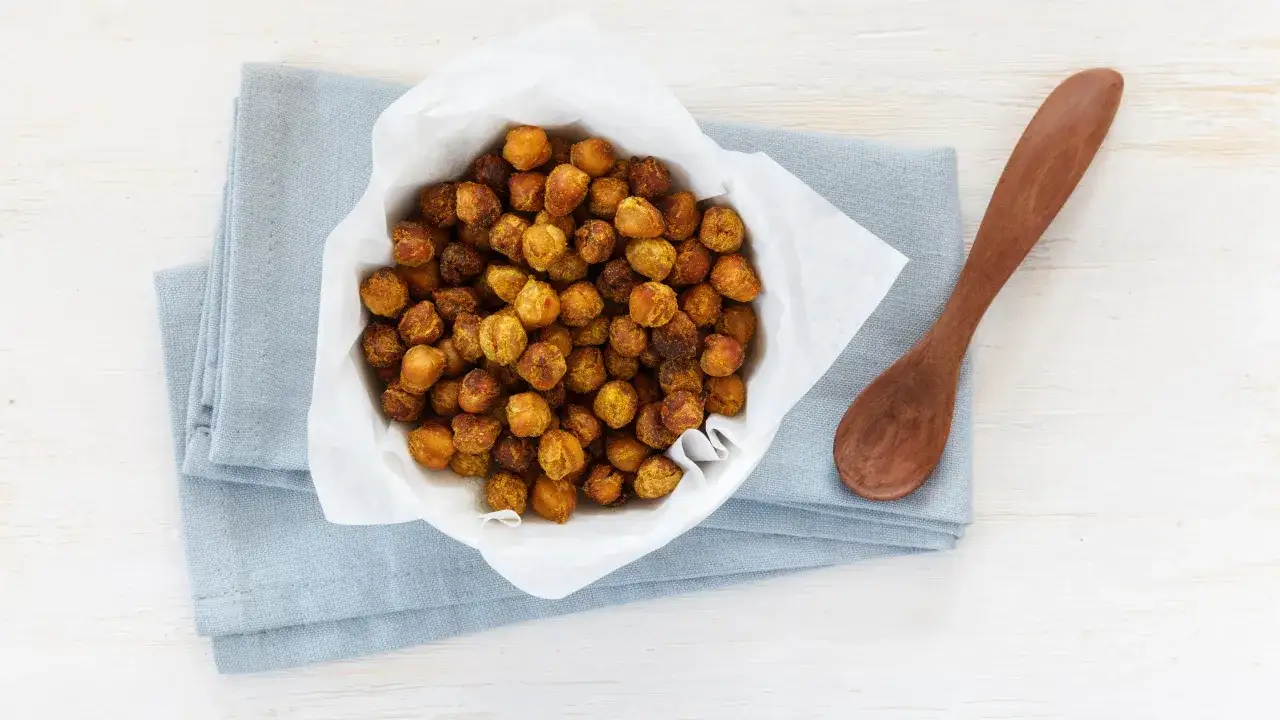 Bol de pois chiches grillés, parfaits pour manger avant ou après le sport le soir. Une cuillère en bois est à côté.