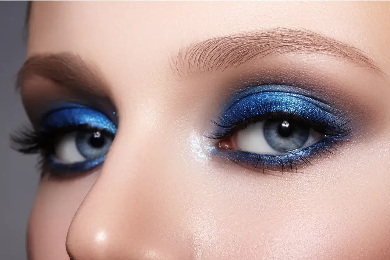 Yeux bleus intenses avec un maquillage smoky eye audacieux et scintillant.