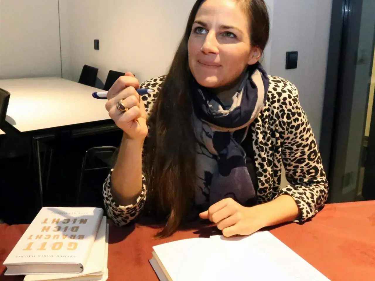 Esther Maria Magnis hält einen Stift, ihr Blick ist nachdenklich. Neben ihr liegt ihr Buch