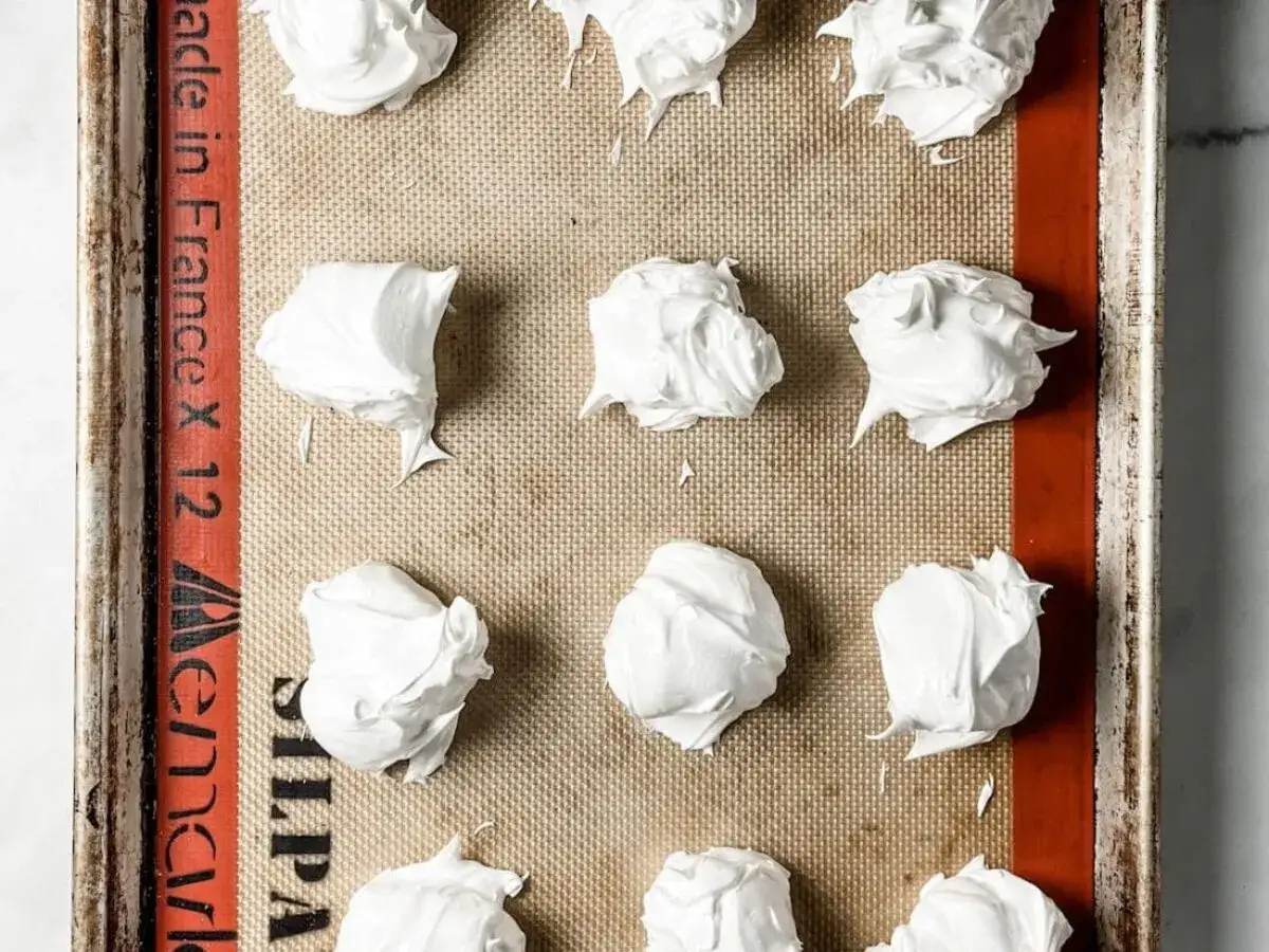 Petites meringues italiennes prêtes à cuire sur une plaque recouverte de papier sulfurisé.