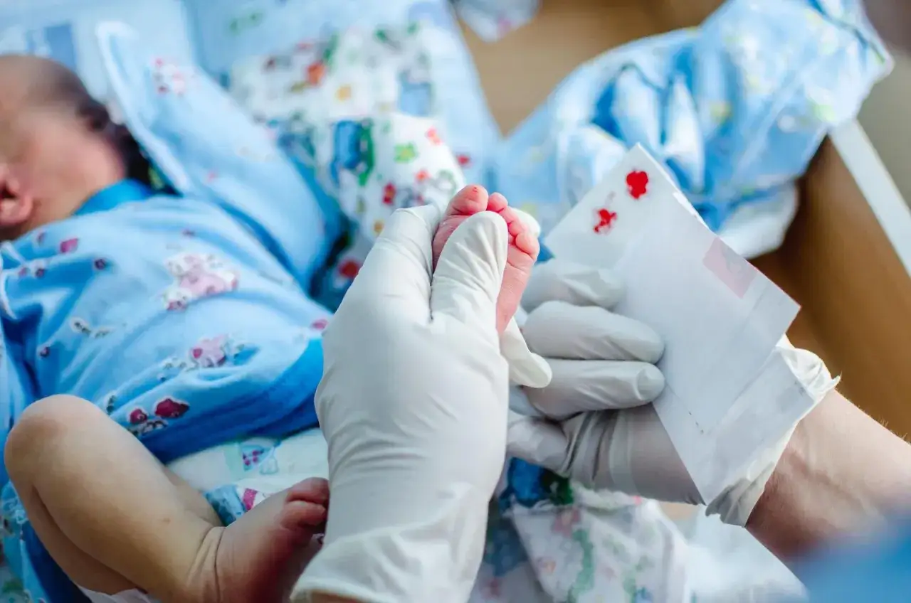 Pobieranie próbki krwi do badań CRP u noworodka. Delikatne paluszki stópki maluszka i biała bibułka z kroplami krwi.