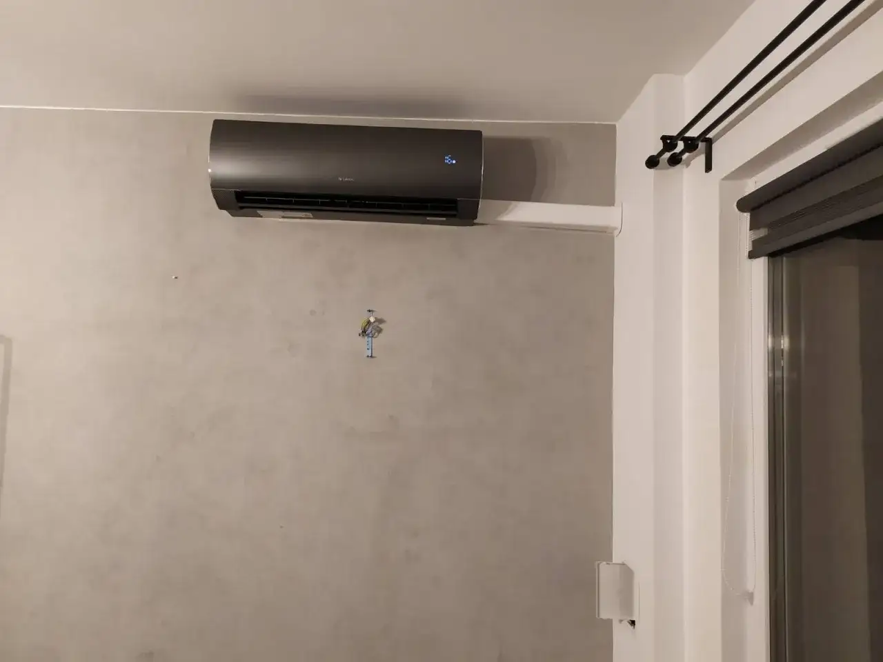 Nowoczesna klimatyzacja ścienna w kolorze grafitowym, zamontowana na szarej ścianie.