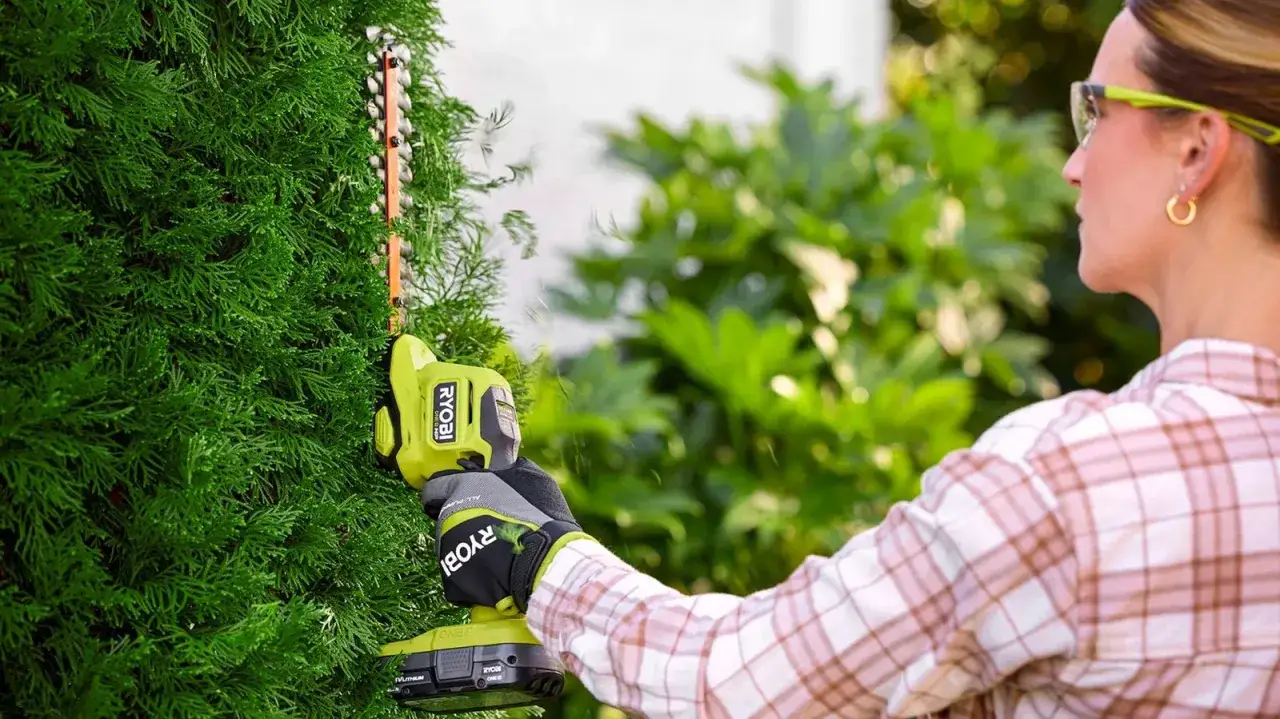 Une femme taille une haie avec un taille-haie électrique. La batterie 2Ah offre une excellente autonomie pour un jardinage sans fil.