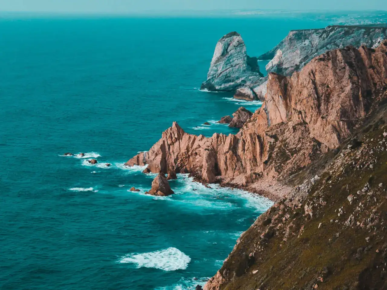 Steile Felsklippen und das türkisfarbene Meer an der Küste der Lissabon Umgebung. Wellen schlagen gegen die Felsen.