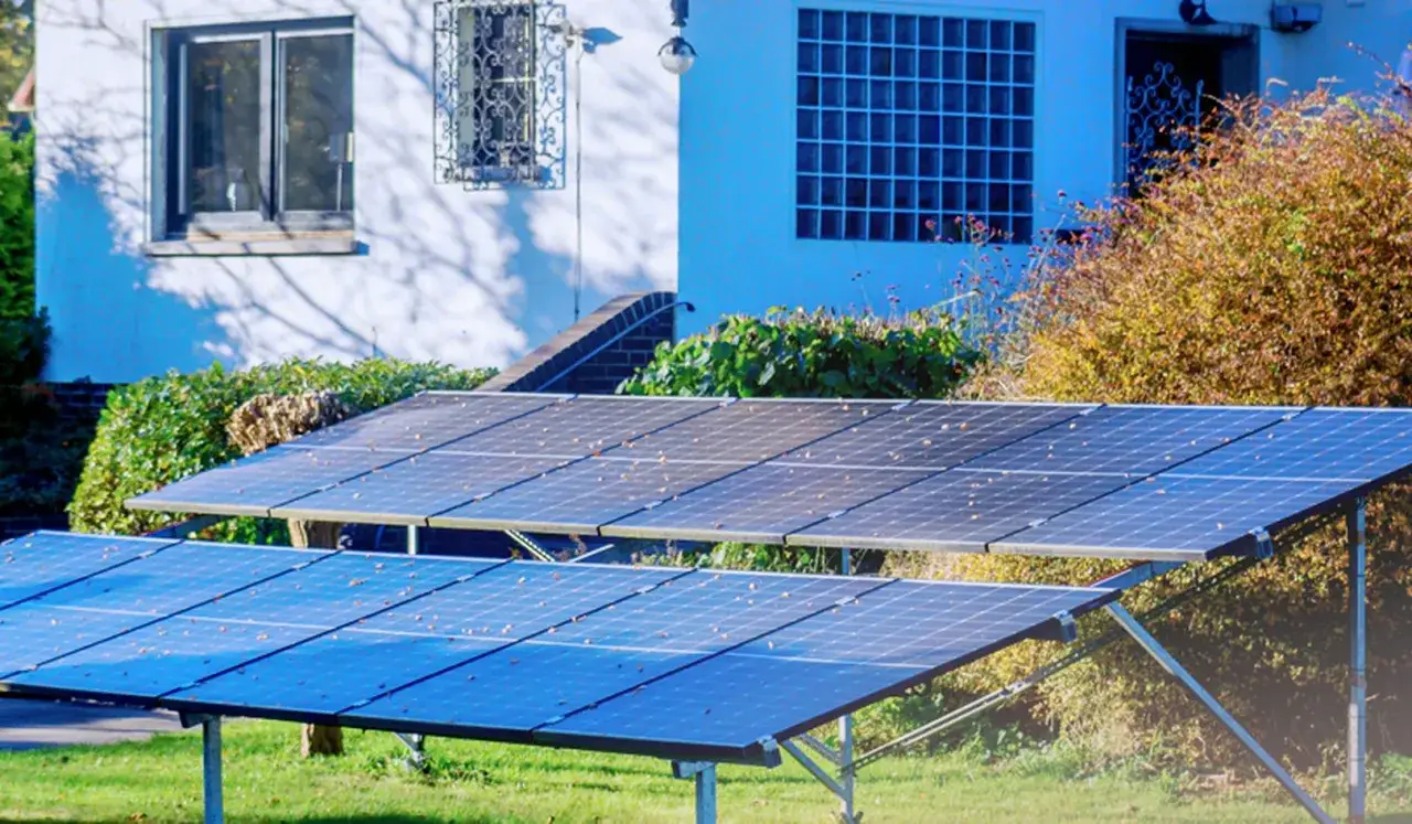 Dwa rzędy paneli fotowoltaicznych na trawniku przed domem. Instalacja PV zbiera energię słoneczną.