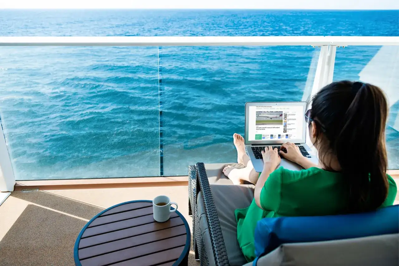 Donna su balcone con laptop, mare blu sullo sfondo. Scopri il pacchetto wifi MSC e il suo costo per restare connesso.