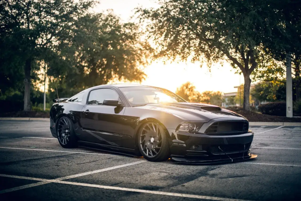Czarny Ford Mustang na parkingu, zachód słońca tworzy ciepłą poświatę. Ta fotografia samochodowa uchwyciła moc i styl.