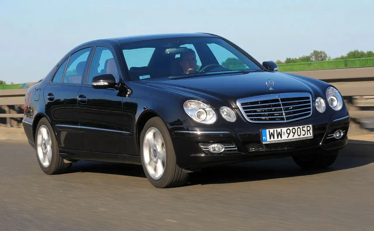 Czarny w211 mercedes z kierowcą jedzie po drodze.