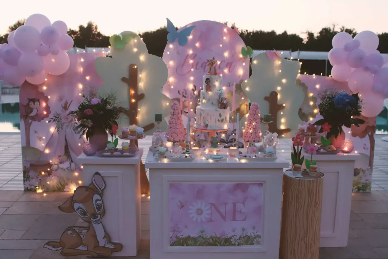 Un allestimento incantevole per un battesimo: torta a più piani, dolcetti, palloncini rosa e decorazioni a tema bosco incantato.