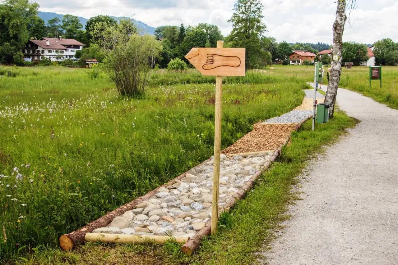 Barfu&szlig;pfad am bayerischen See mit Schild, das einen Fu&szlig;abdruck zeigt. Steine, Holzsp&auml;ne und Kies laden zum Gehen ein.