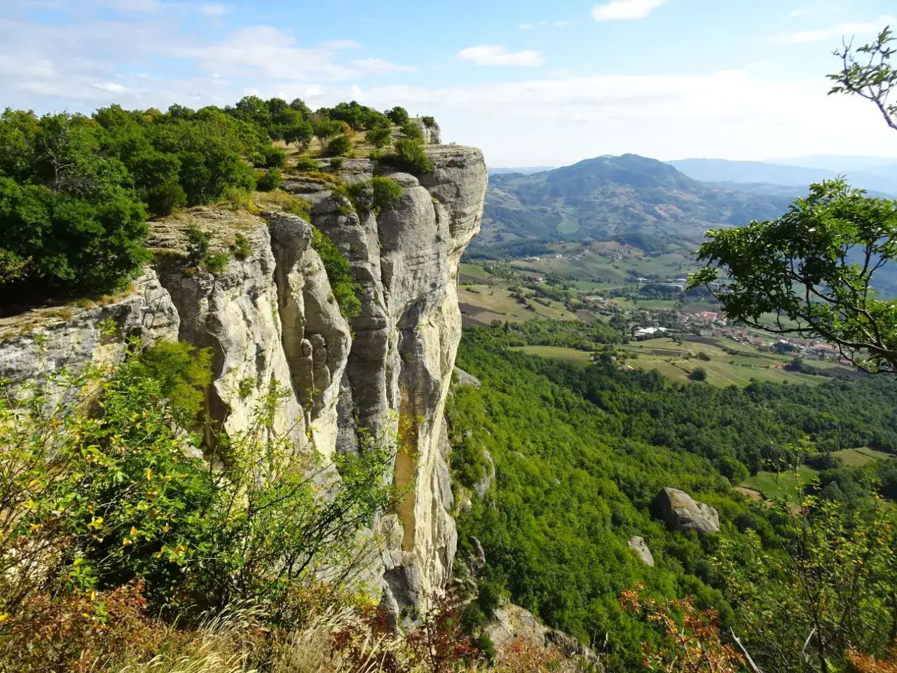 Imponente parete rocciosa della Pietra di Bismantova, con vegetazione lussureggiante e un panorama collinare sullo sfondo.