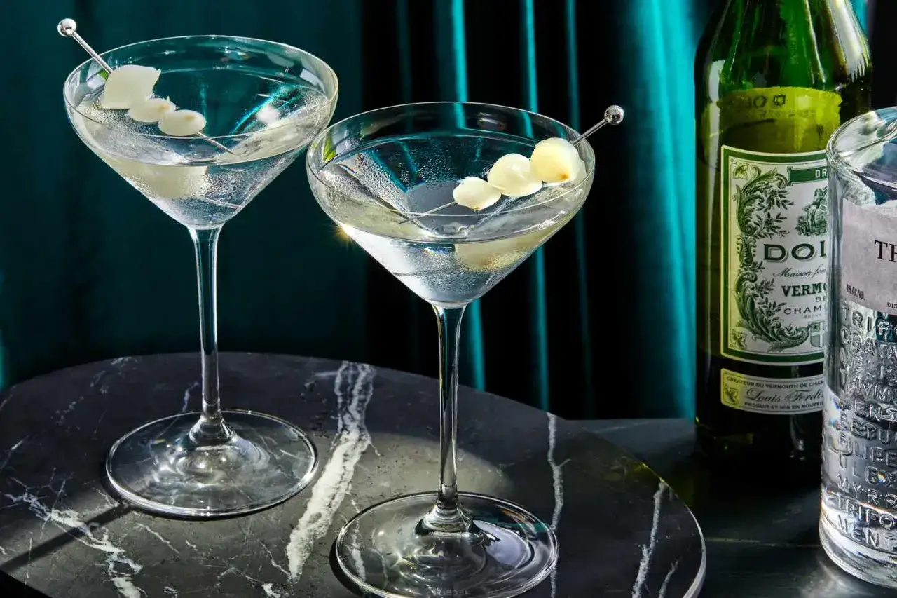 Dwa eleganckie martini z oliwkami, obok butelka wermutu. Idealne na wieczór, by dowiedzieć się, jak zrobic martini.