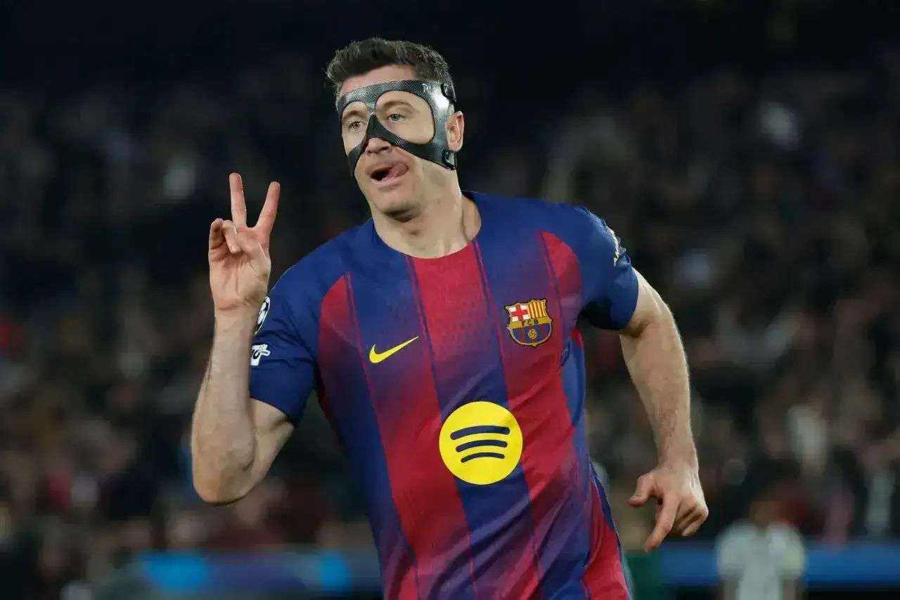 Robert Lewandowski w masce ochronnej, z dwoma palcami uniesionymi w geście zwycięstwa. Jego wzrost i determinacja na boisku budzą podziw.