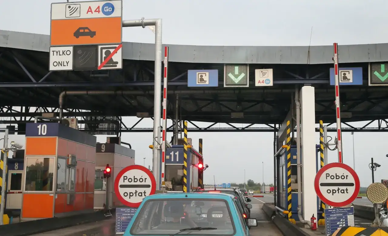 Kolejka samochodów na placu poboru opłat A4. Znaki informują o możliwości płatności i dostępnych pasach.