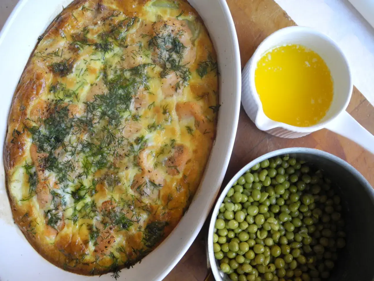 Enkel laxpudding i ugnsform, med en skål smält smör och en kastrull med gröna ärtor.