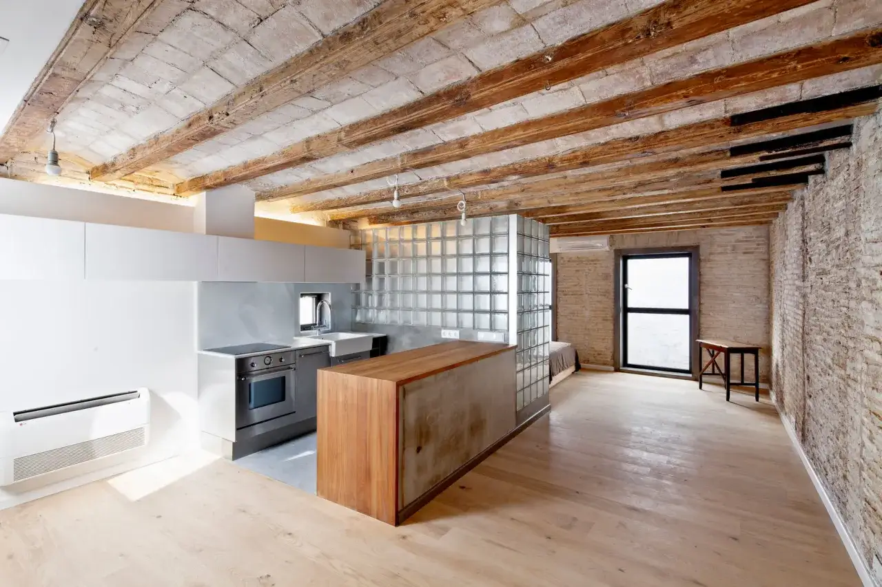 Cocina moderna con isla de madera y cristal, techos de vigas expuestas. Un espacio abierto que evoca la idea de como tirar un tabique para crear amplitud.