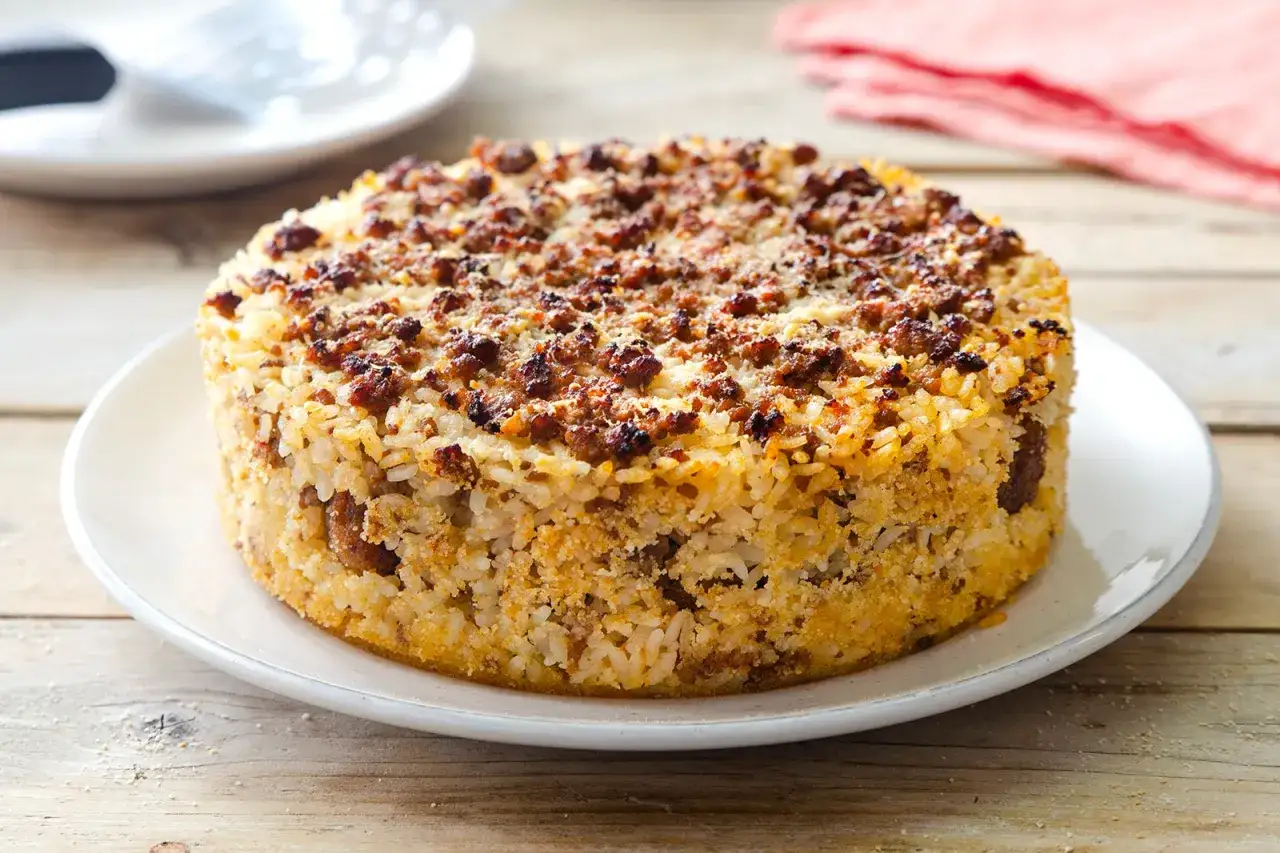 Timballo di riso dorato con carne macinata croccante in cima, servito su un piatto bianco.