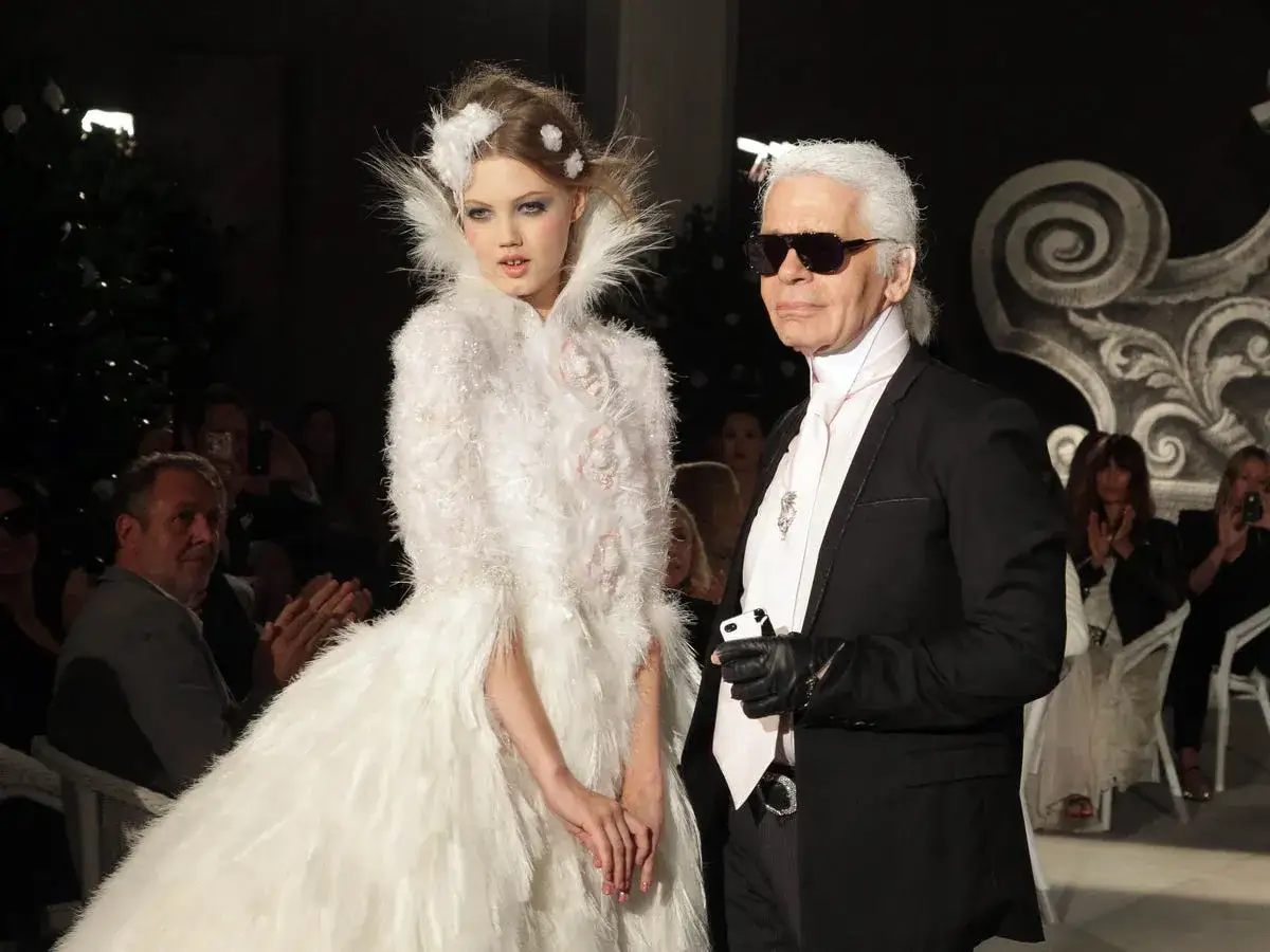 Karl Lagerfeld, jeden z najsłynniejszych projektantów mody, obok modelki w białej, puszystej kreacji na pokazie.