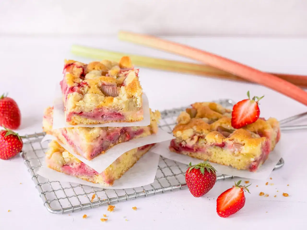 Saftiger Erdbeer Rhabarber Kuchen mit Streuseln, garniert mit frischen Erdbeeren und Rhabarberstangen.