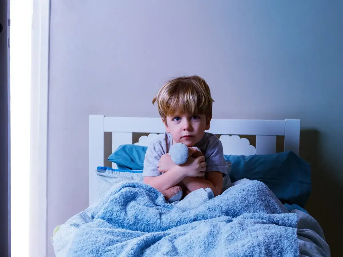 Mi hijo de 2 a&ntilde;os no quiere dormir. Est&aacute; sentado en la cama, abrazando un peluche, con los ojos bien abiertos y una expresi&oacute;n seria.