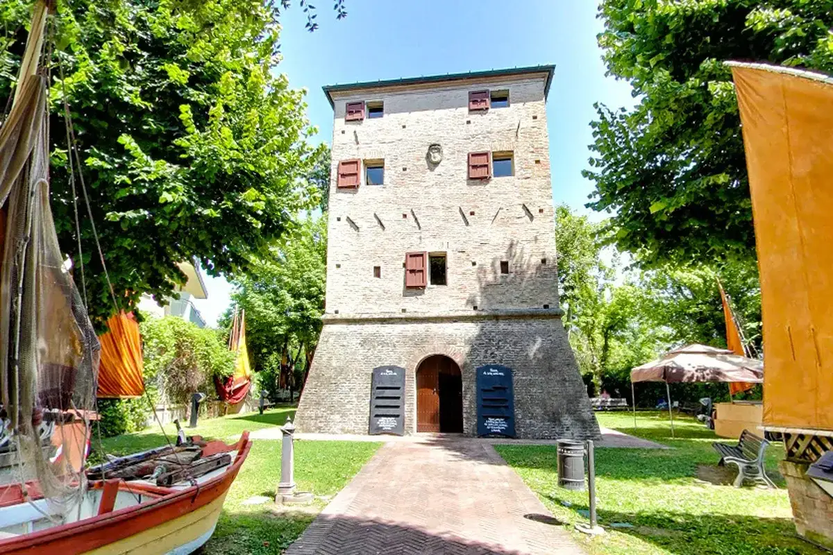 Torre antica con vele di barche e alberi verdi, un luogo che evoca la storia marittima e l'anima di Igea Marittima.