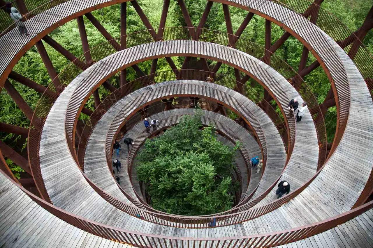 Une promenade en spirale en bois dans une forêt, idéale pour savoir que faire au Danemark. Des gens explorent cette structure unique.