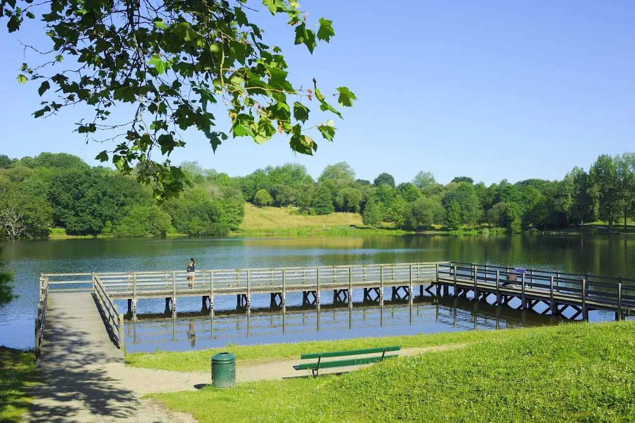 Un ponton en bois traverse le lac Marion à Biarritz, bordé d'arbres verdoyants sous un ciel bleu.