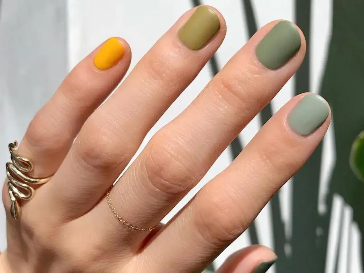 Main gauche ornée de bijoux dorés et d'un nail art dégradé de couleur, passant du jaune vif au vert olive.