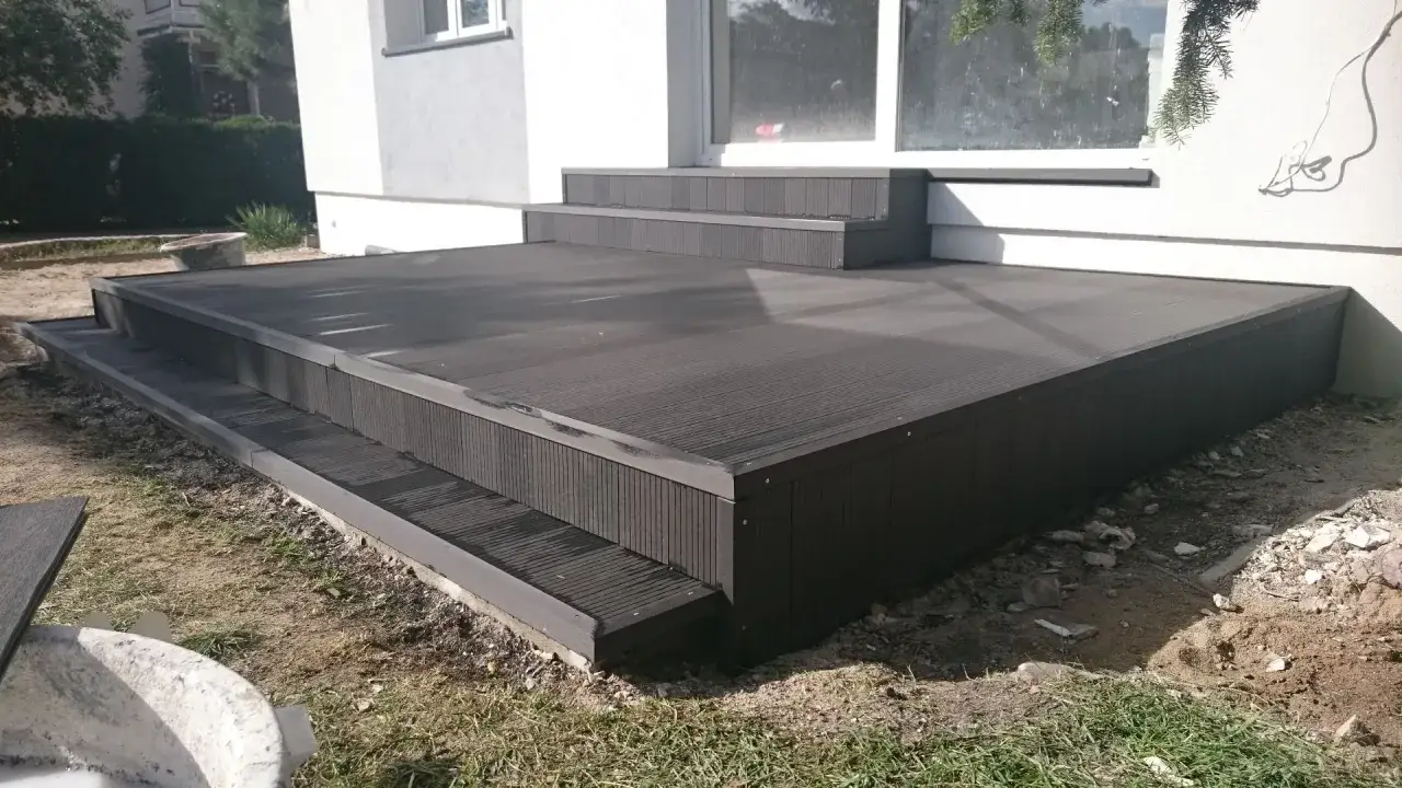 Nowy taras z ciemnego kompozytu z dwoma stopniami, idealny do nowoczesnego ogrodu.
