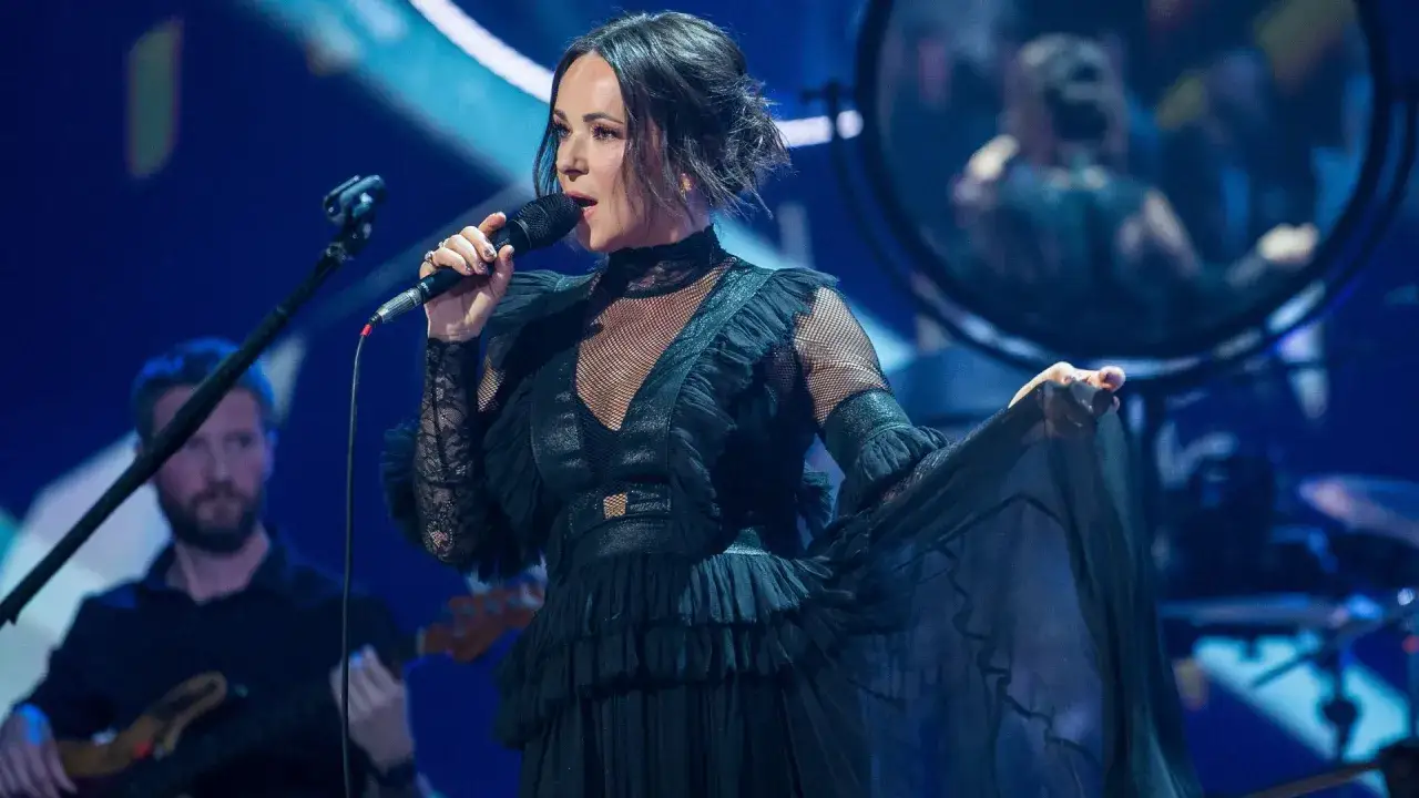 Kasia Kowalska w czarnej, falbaniastej sukni śpiewa na scenie, wykonując swoje utwory.