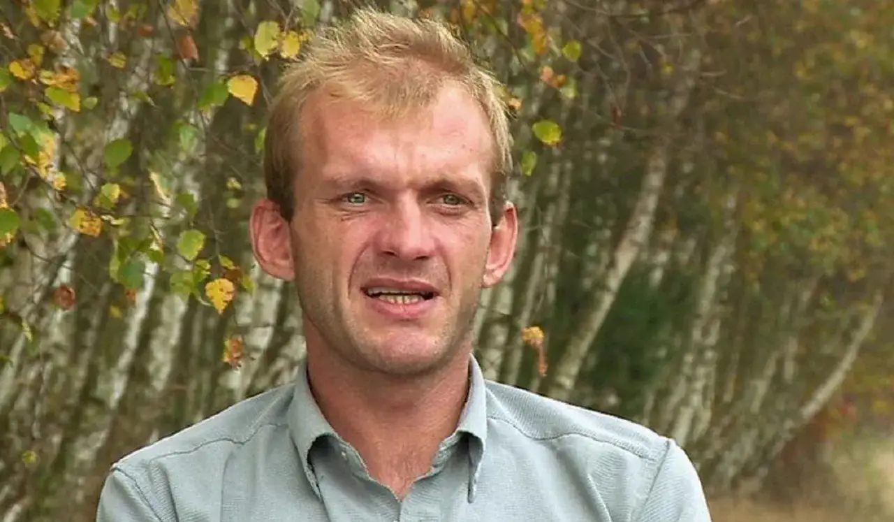 Ryszard Szczena, mężczyzna z blond włosami, w jasnej koszuli, na tle jesiennego lasu.