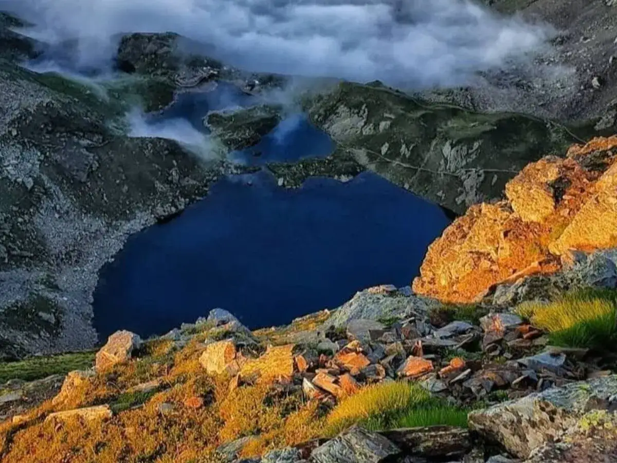 Atardecer dorado ilumina las rocas y la hierba junto a los ibones de Benasque, con el agua azul profundo reflejando las nubes.