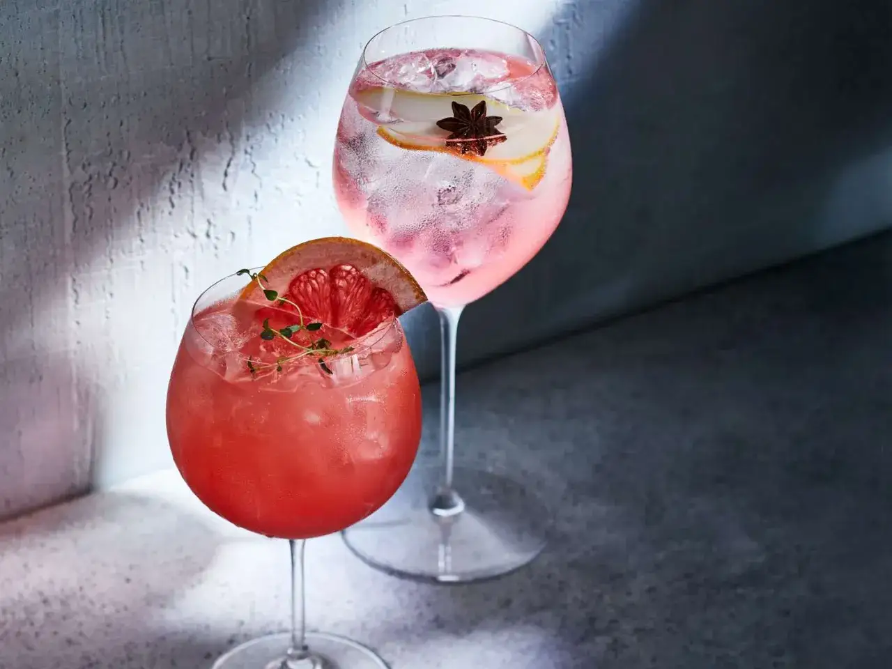 Två glas med rosa drinkar, en garnerad med grapefrukt och en med stjärnanis och citrus.