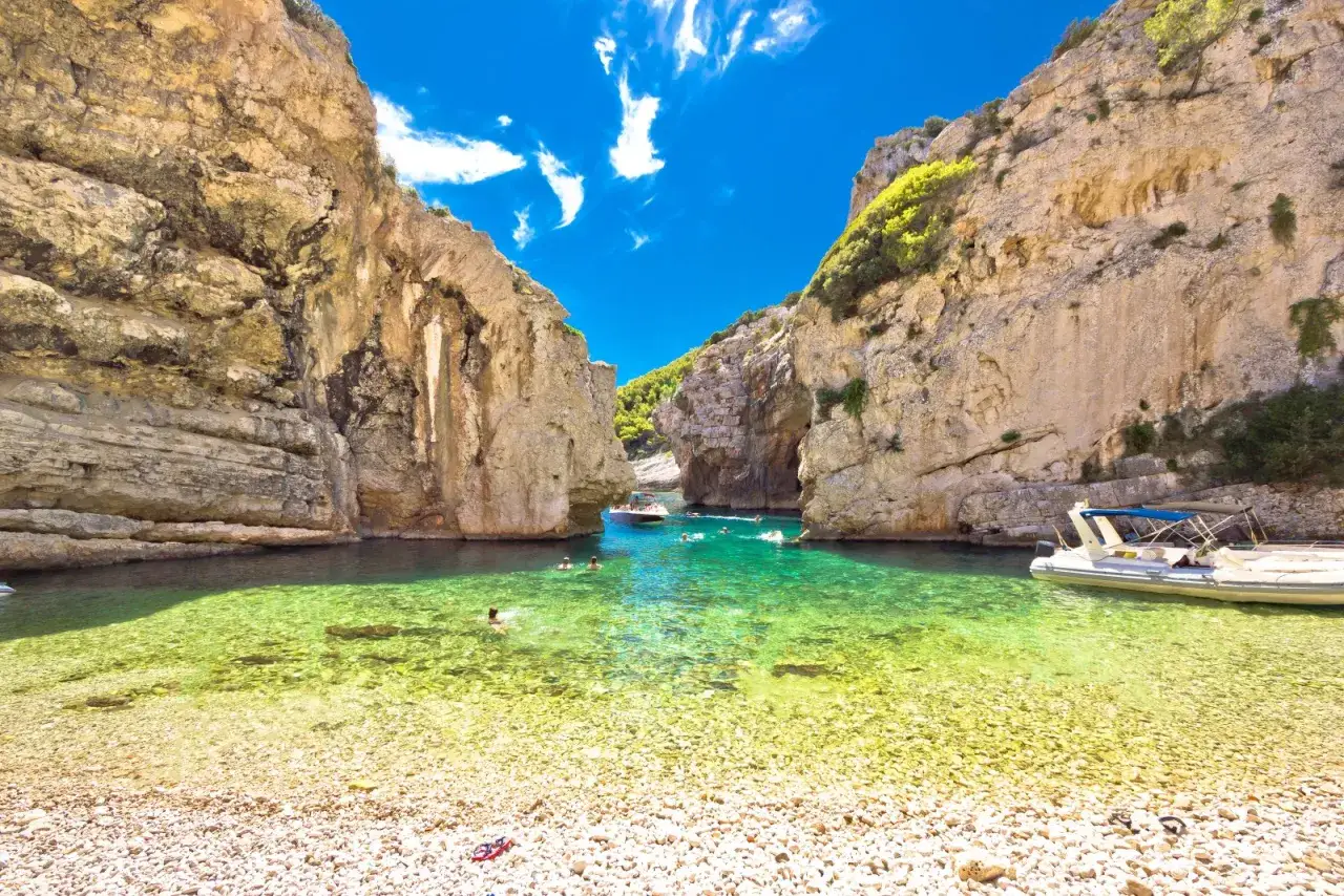 Baia cristallina con scogliere imponenti, barche e bagnanti che si godono il sole. Un angolo di paradiso sull'isola di Lissa.