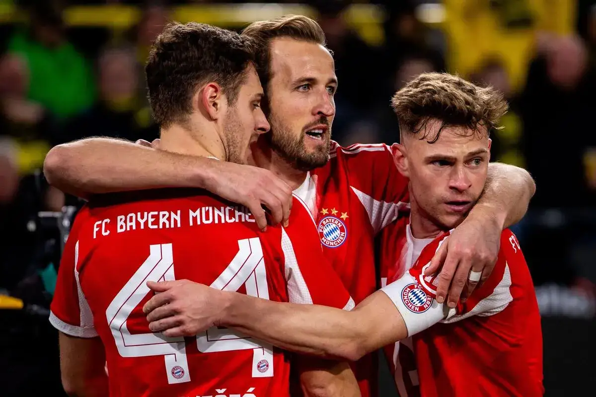 Trzech piłkarzy Bayernu Monachium w czerwonych koszulkach, z ramionami na sobie. Harry Kane w środku. To obraz, który może symbolizować udane bayern monachium transfery.