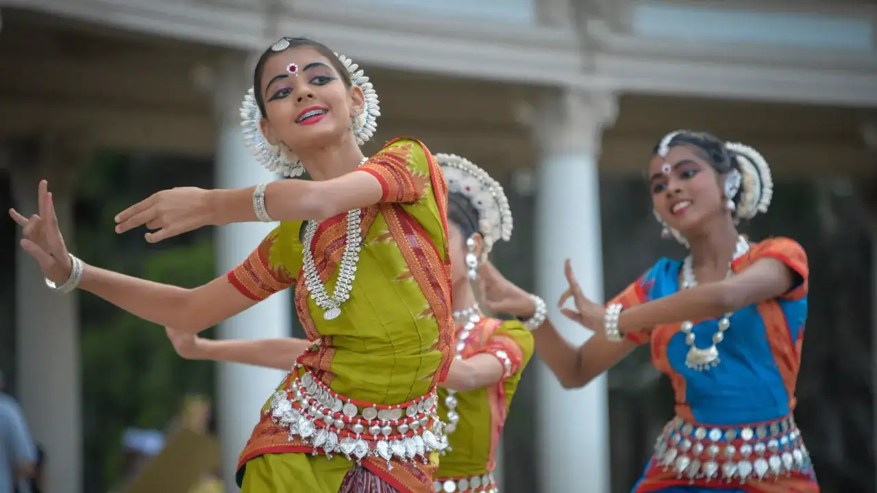 Młode tancerki w barwnych strojach, przypominających styl **bollywood**, wykonują tradycyjny taniec.