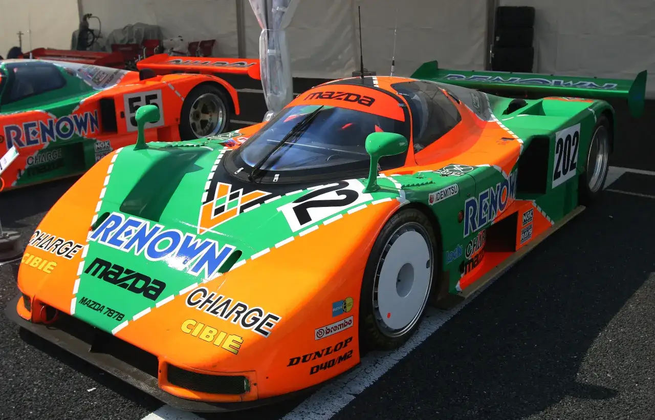 El ic&oacute;nico Mazda 787B, con sus vibrantes colores naranja y verde, listo para la carrera.