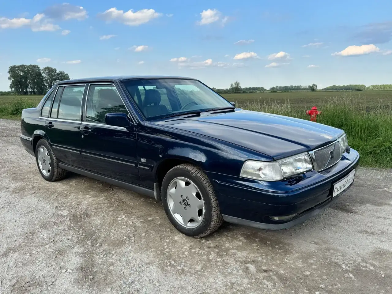 Ciemnoniebieskie volvo stare modele, klasyk na tle pól i błękitnego nieba.