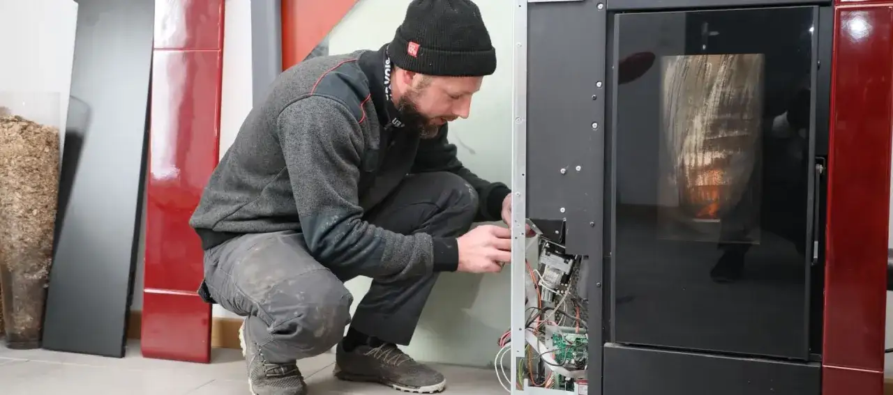 Tecnico al lavoro per la riparazione stufe a pellet. Si intravedono componenti interni e la fiamma.
