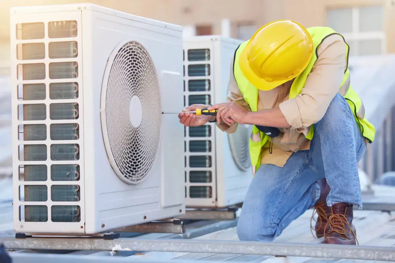 Technicien en jaune, ajustant un climatiseur extérieur. Il s'assure que le **clim souffle chaud** et froid pour le confort de tous.