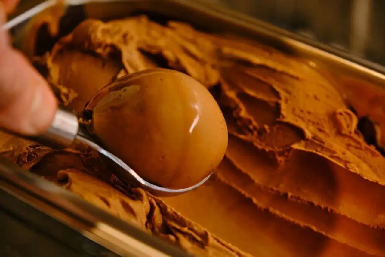 Eine Eiskugel wird aus einer Schale mit cremigem, italienischem Schokoladeneis gesch&ouml;pft. Ein k&ouml;stliches Rezept!